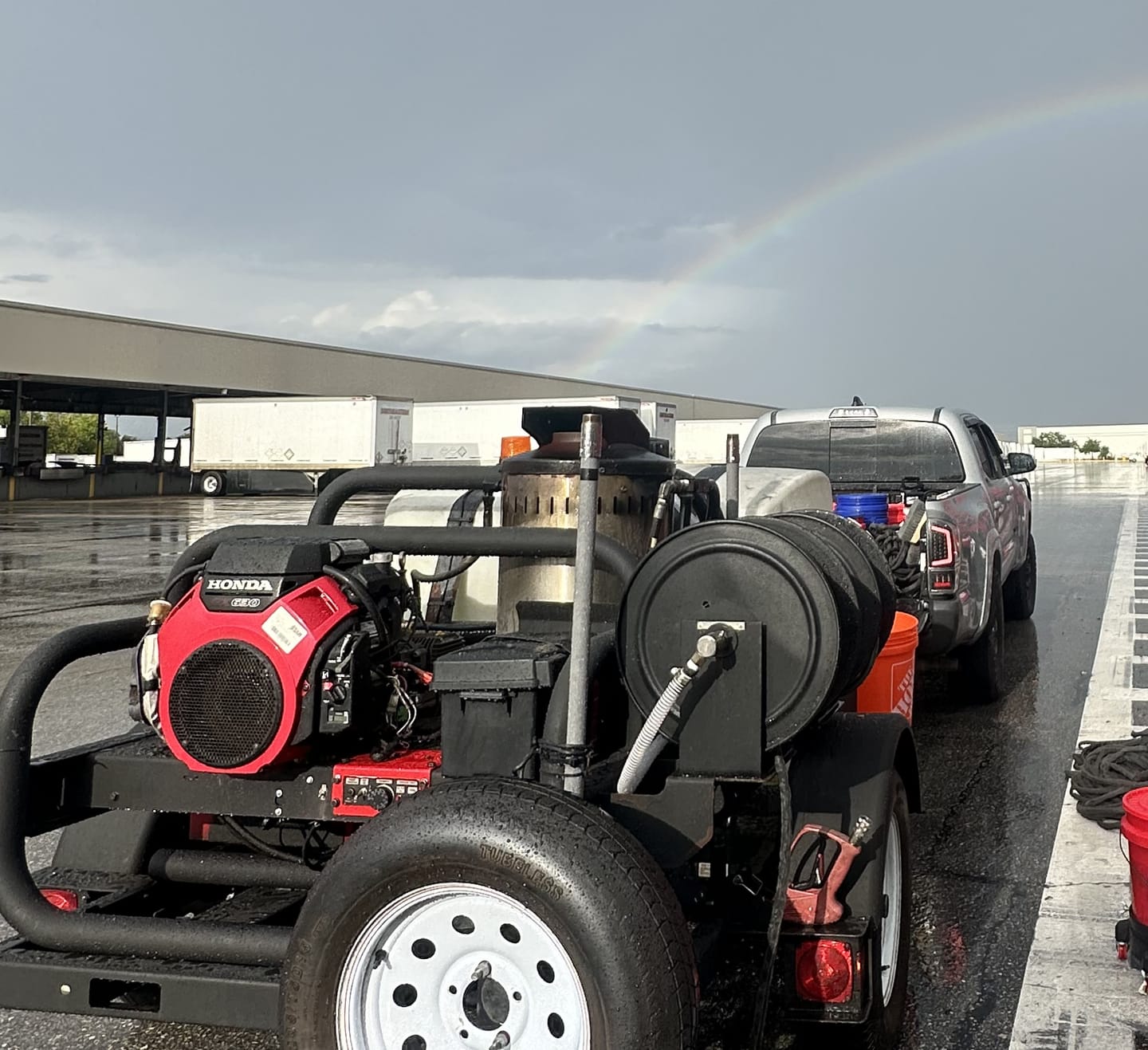 A pressure washing rig on a wet distribution yard under a rainbow after an afternoon storm